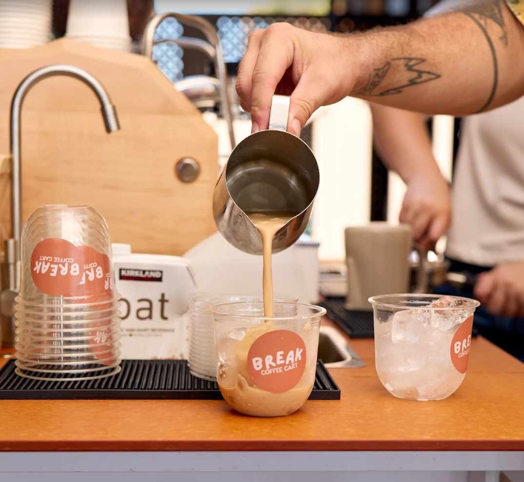 Barista pouring an iced Break Coffee Cart latte at a wellness event